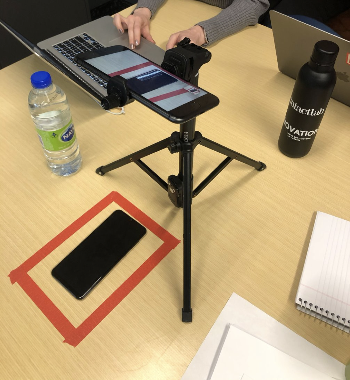 A user-testing rig: phone clamped to a tripod with a camera recording the screen, on a desk